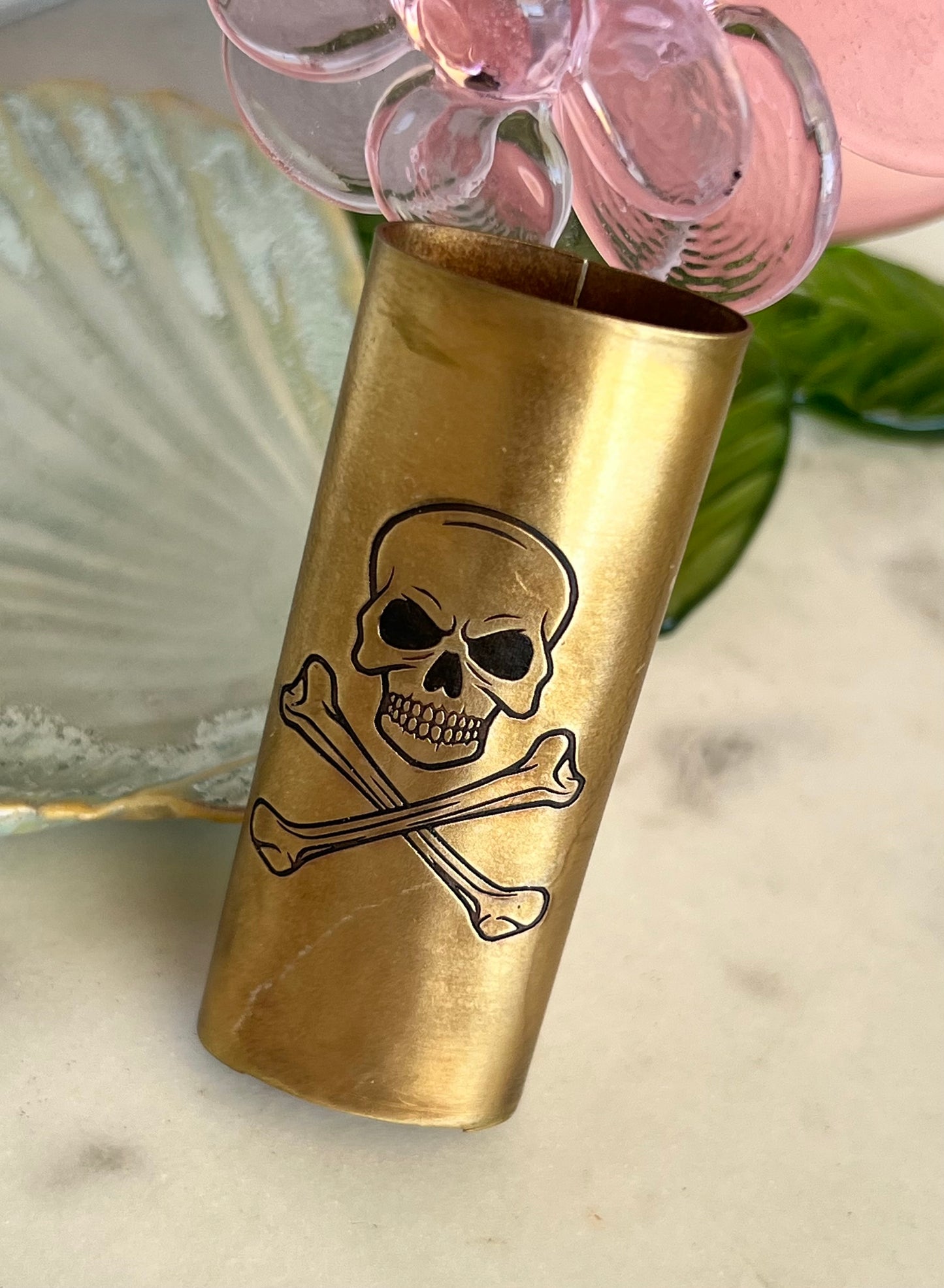 Brass shot glass with skull and crossbones design on a marble surface