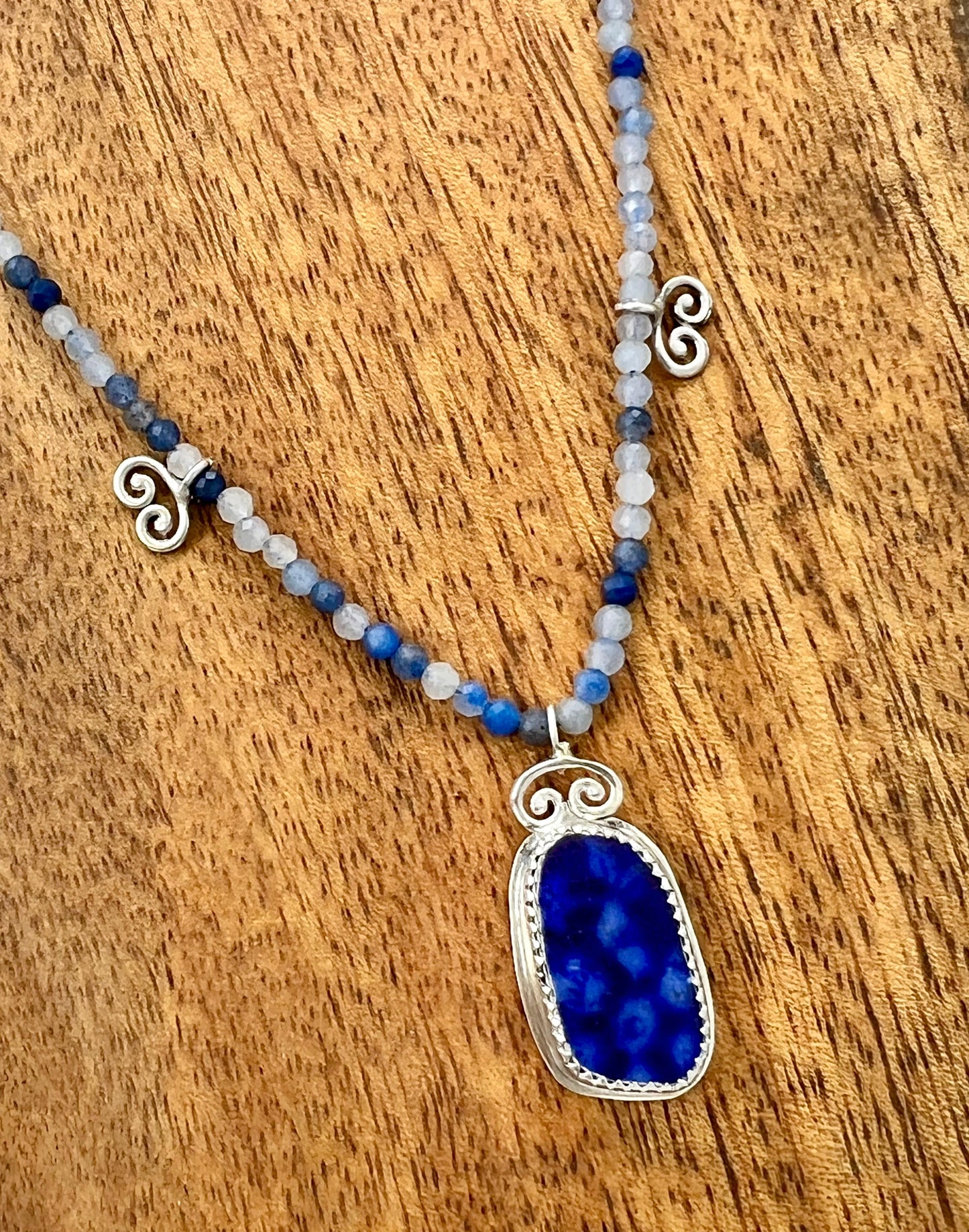 Necklace with blue pendant and beaded chain on a wooden surface