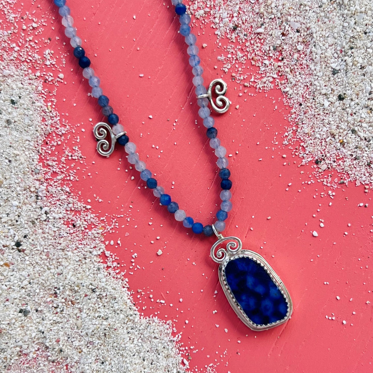 Necklace with blue pendant on a pink and white sand background