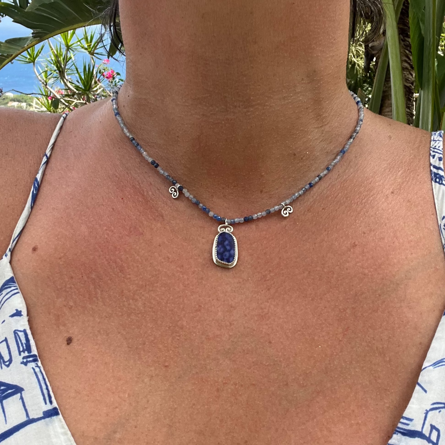 Necklace with a blue pendant worn by a person against a natural background
