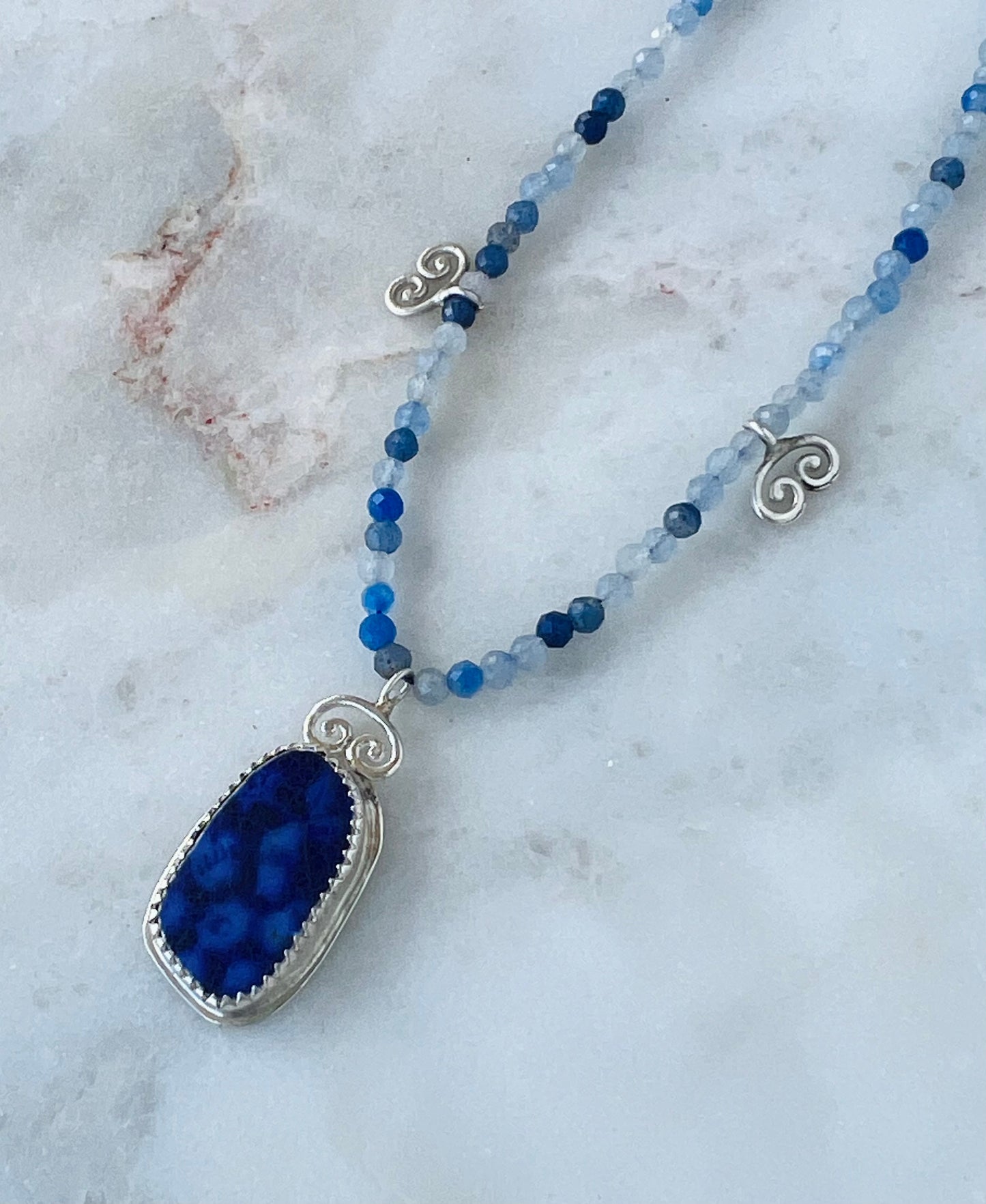 Necklace with blue pendant and beaded chain on a marble surface