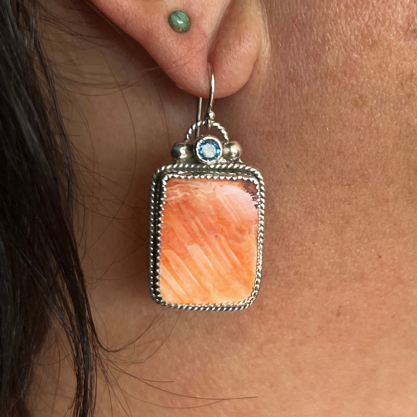 Close-up of an earring with a peach-colored stone worn by a person.