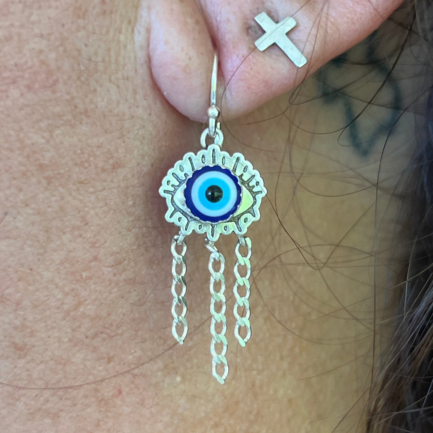 Close-up of an ear with a small gold earring featuring an eye design.