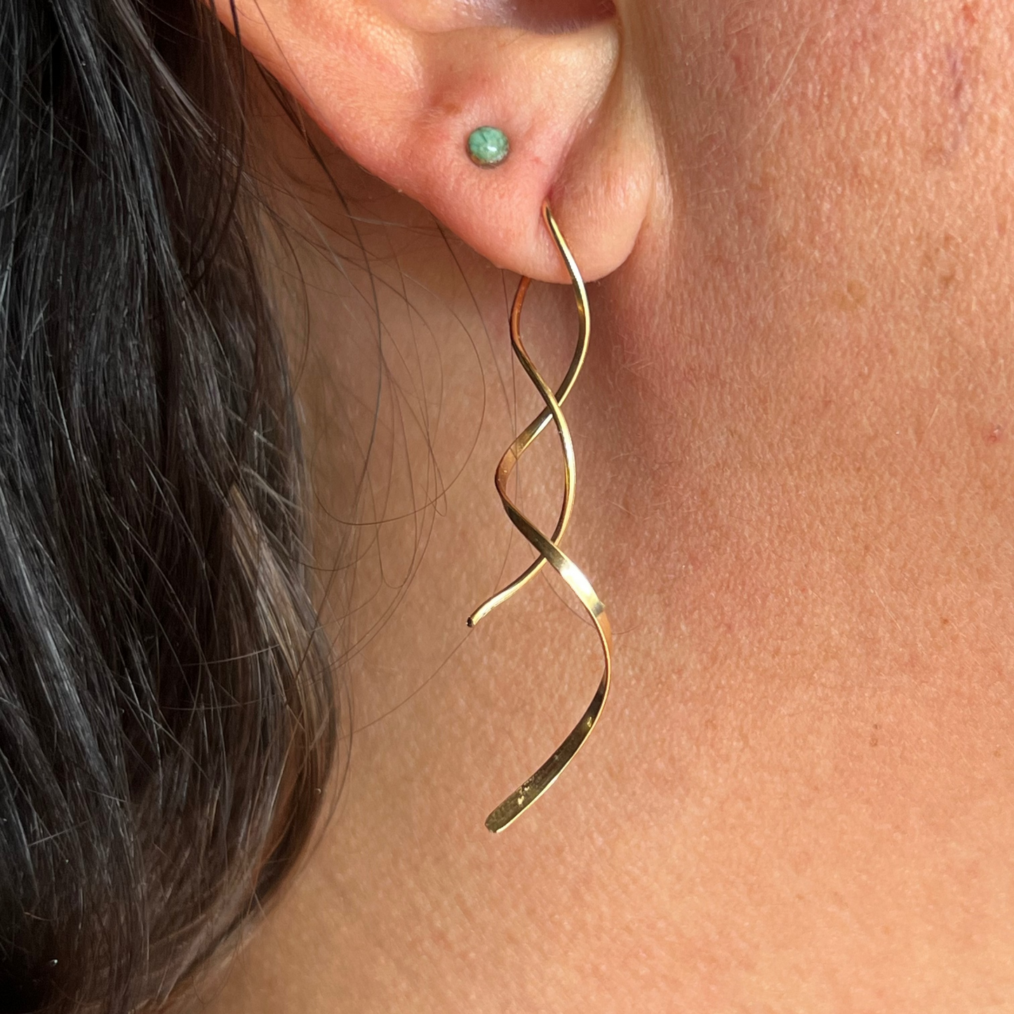 Gold spiral earring worn by a person with dark hair.