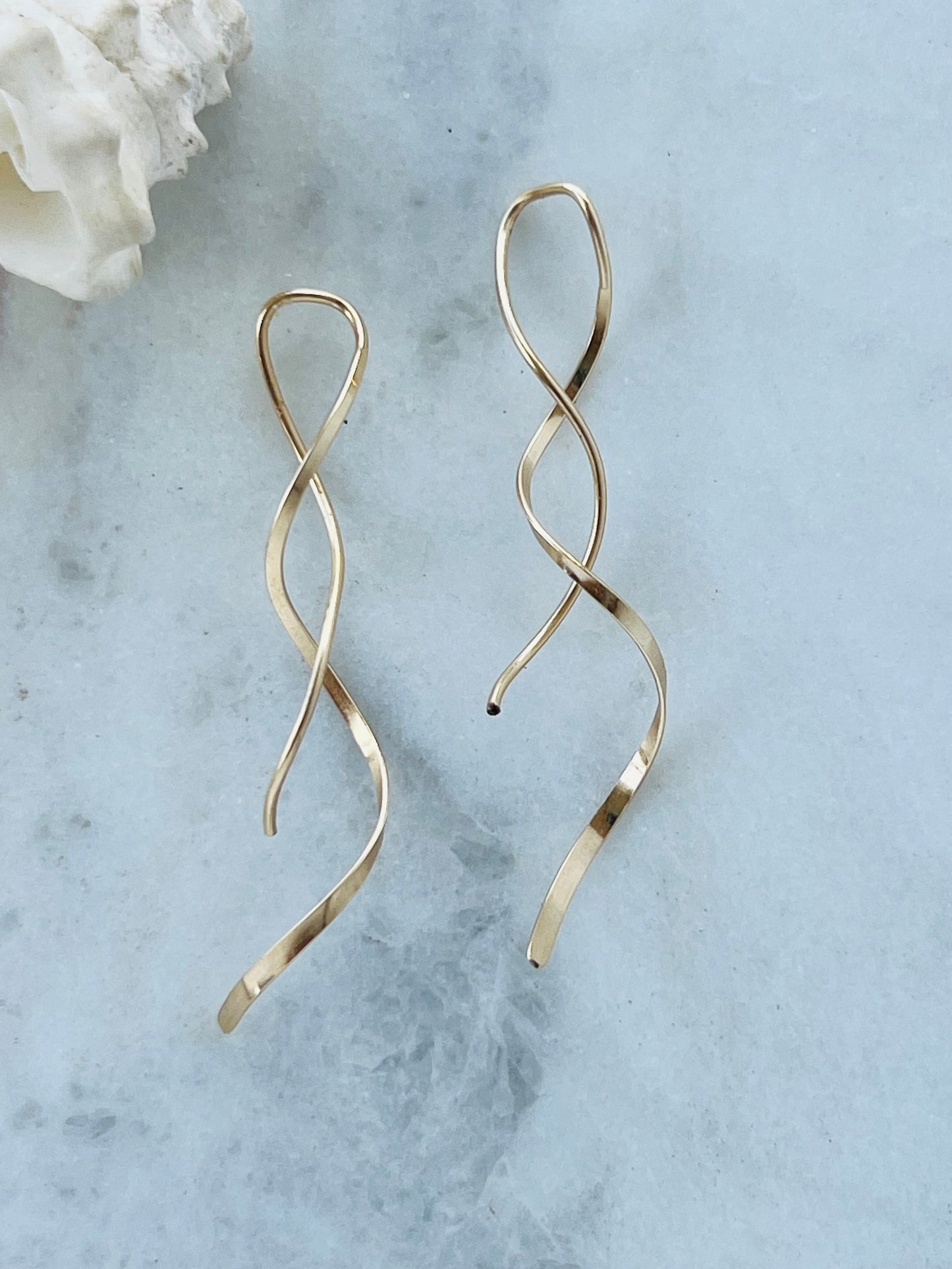 Gold spiral earrings on a light blue marble surface