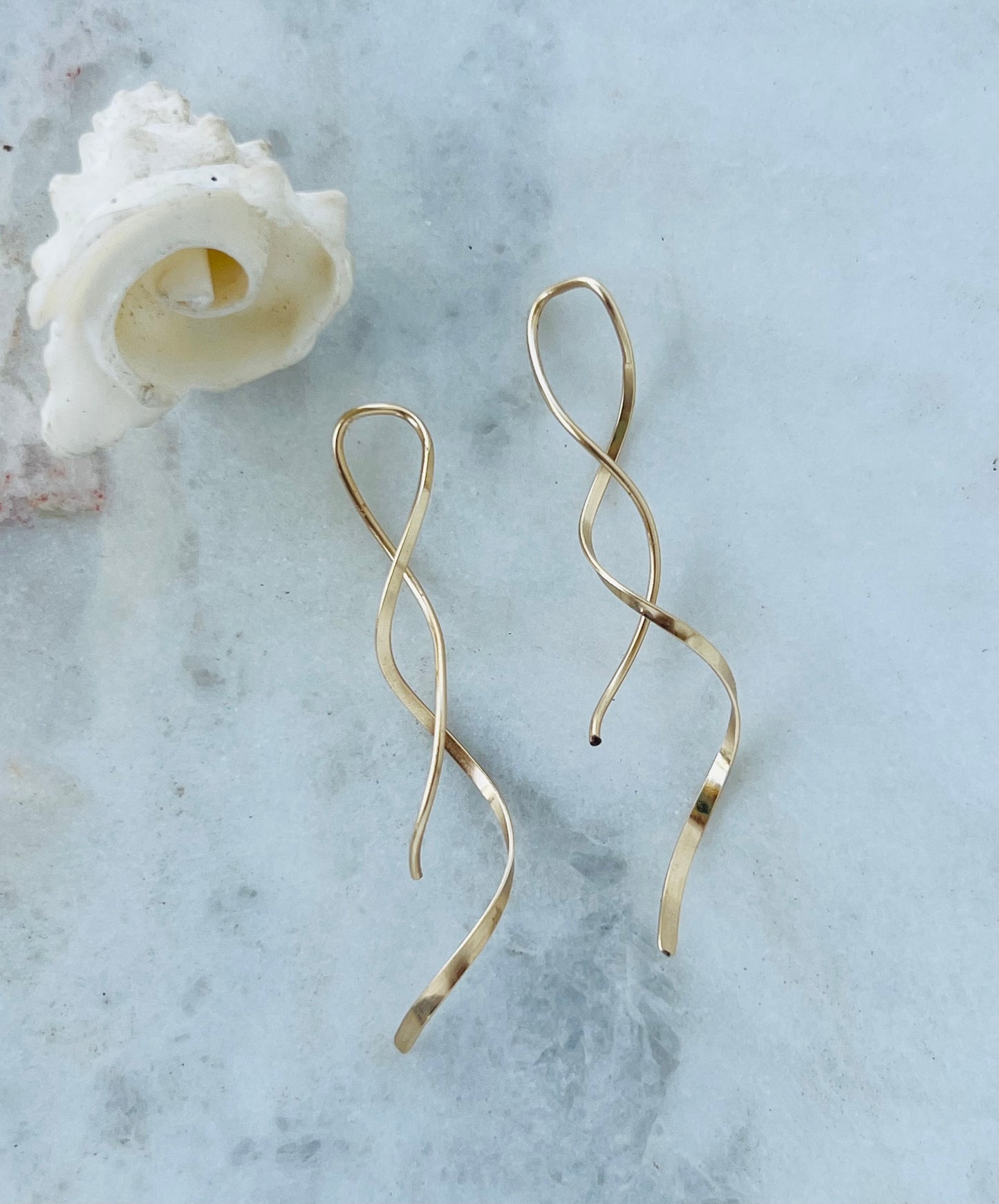 Gold earrings on a marble surface with a shell