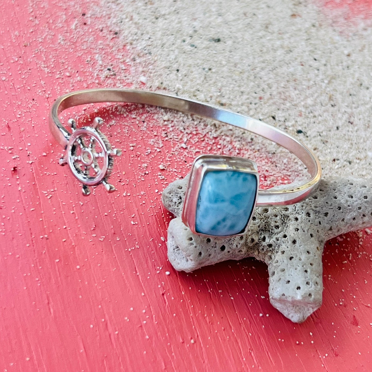 Silver bangle with a blue stone and ship wheel charm on a textured surface