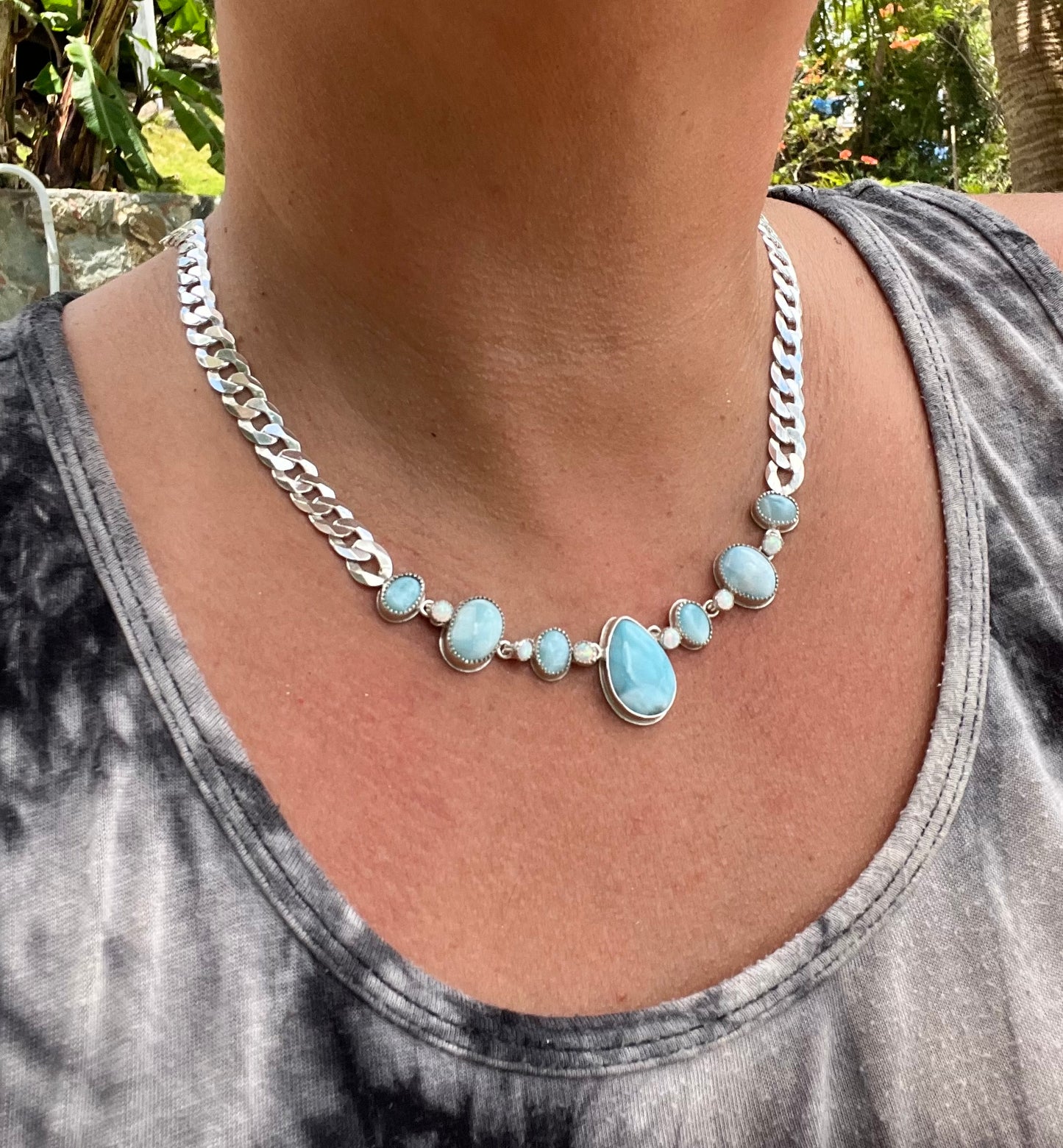 Necklace with blue stones and silver chain worn by a person, with a blurred outdoor background.