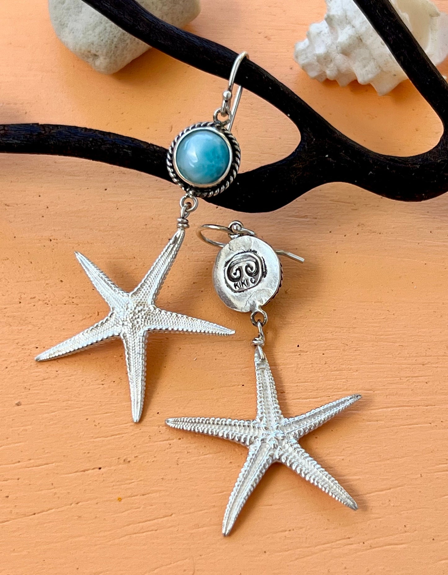 Starfish-shaped earrings with a blue gemstone on a beige surface