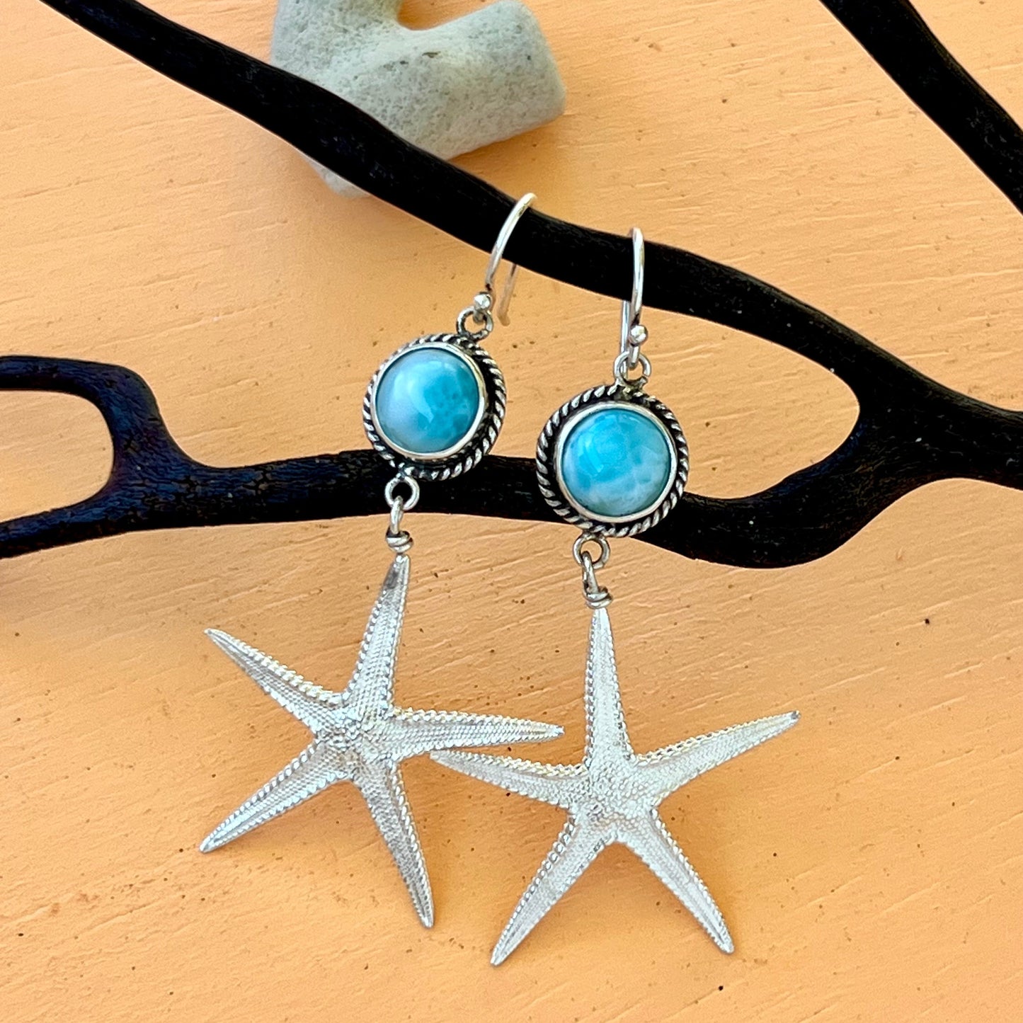 Silver starfish earrings with blue gemstones on a beige background