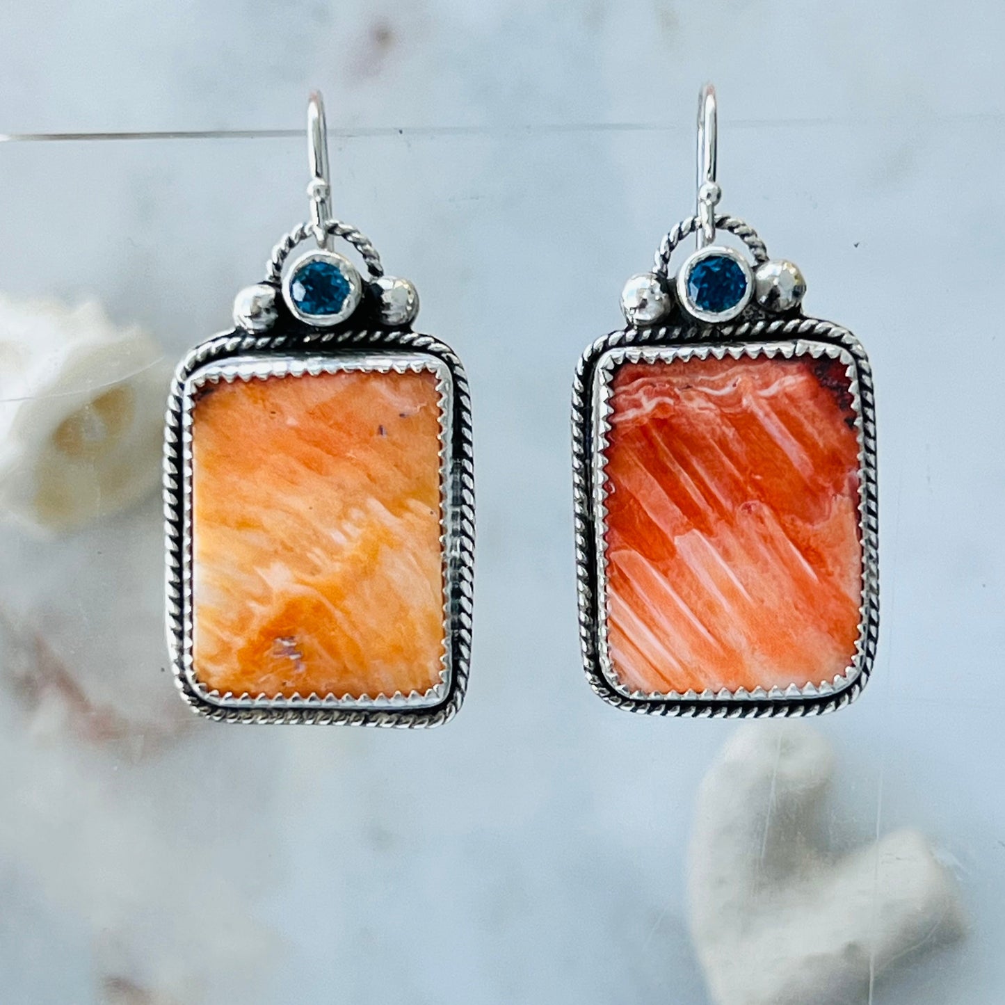 Pair of earrings with orange stone and blue gemstone on a marble background
