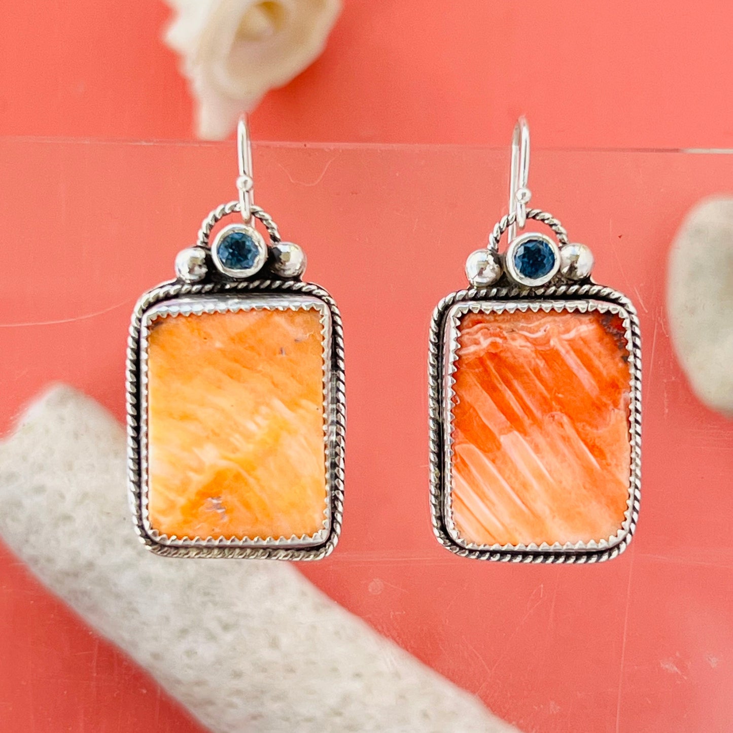 Pair of earrings with orange stone and silver frame on a coral background