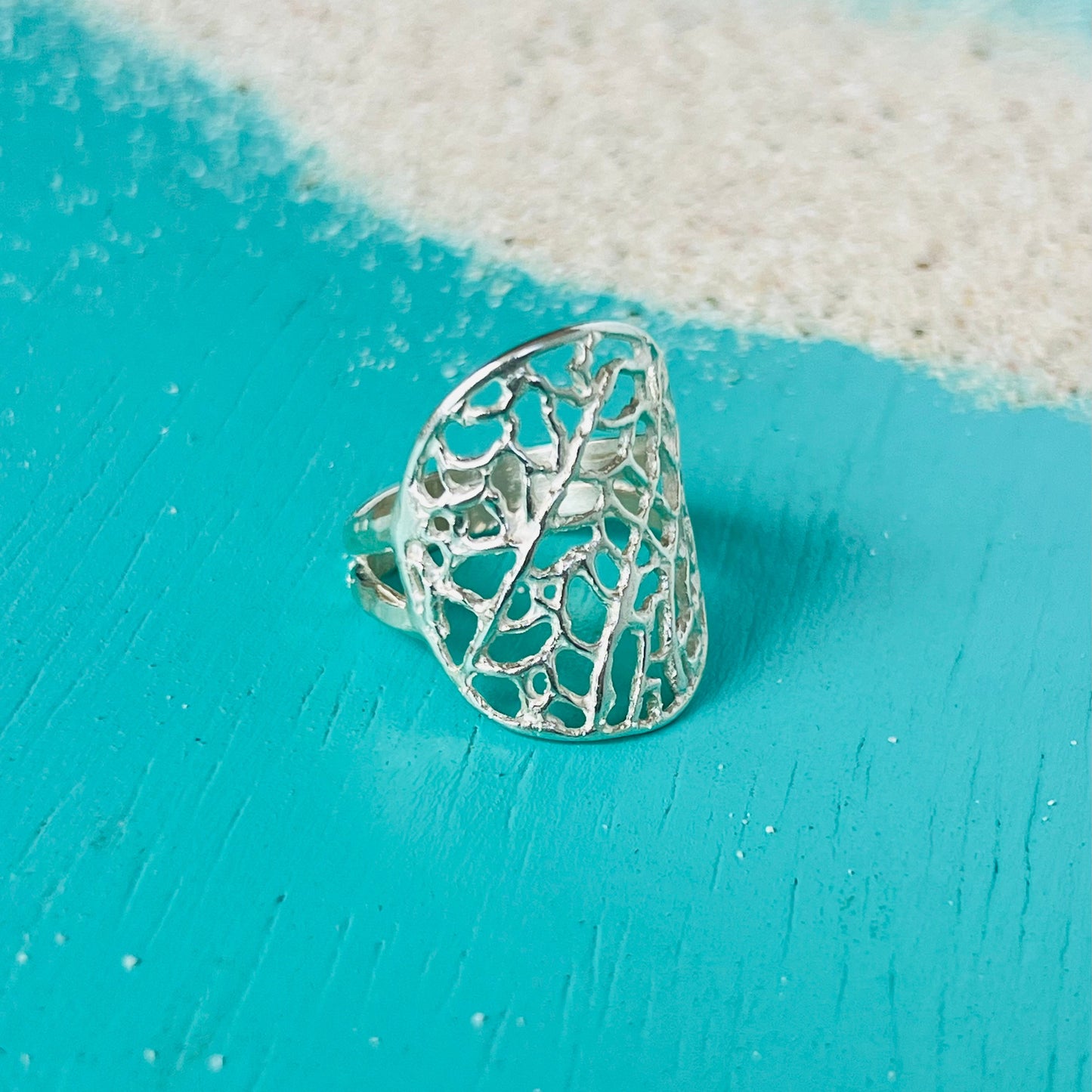 Silver lace ring on a turquoise surface with a white fabric background