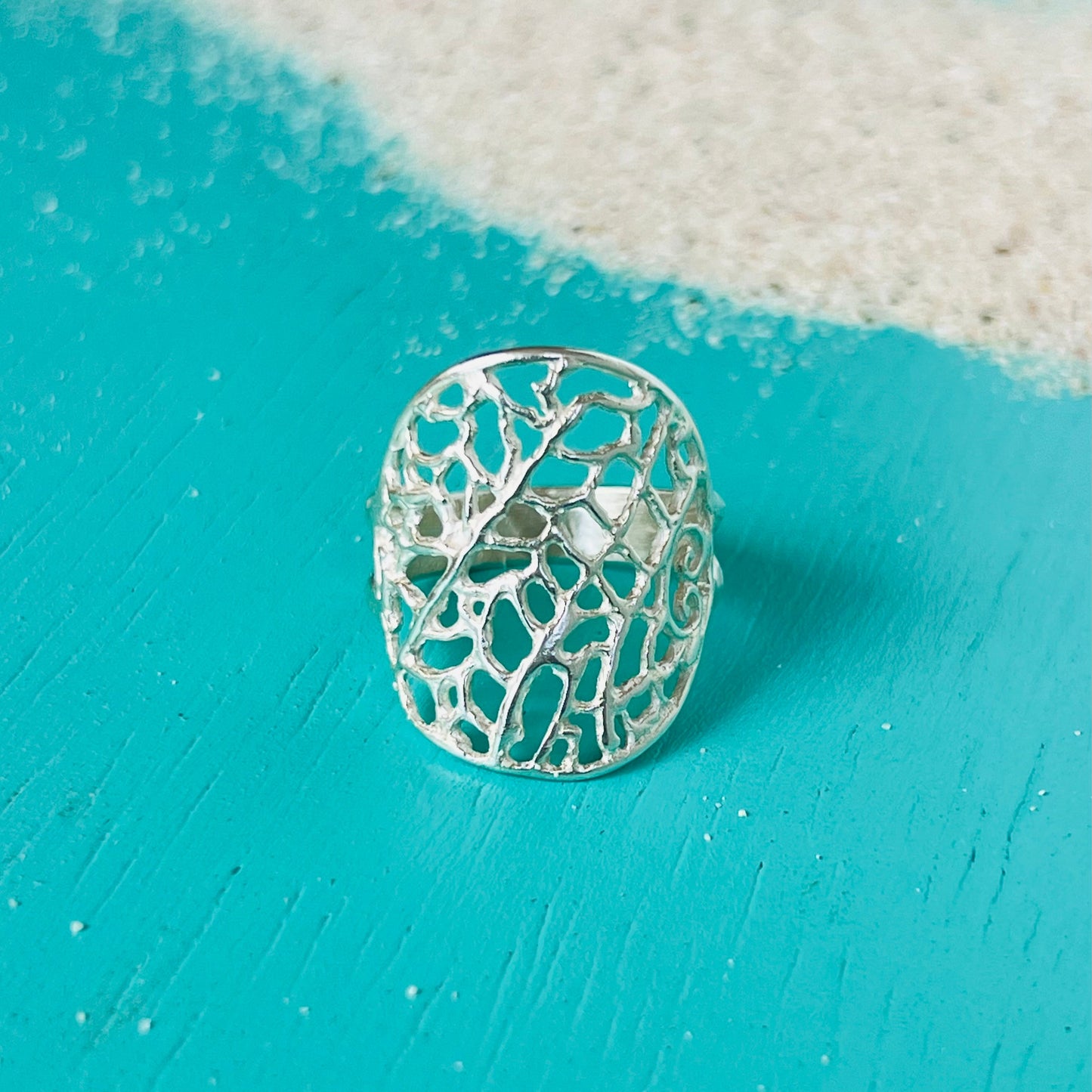 Silver ring with intricate design on a turquoise surface
