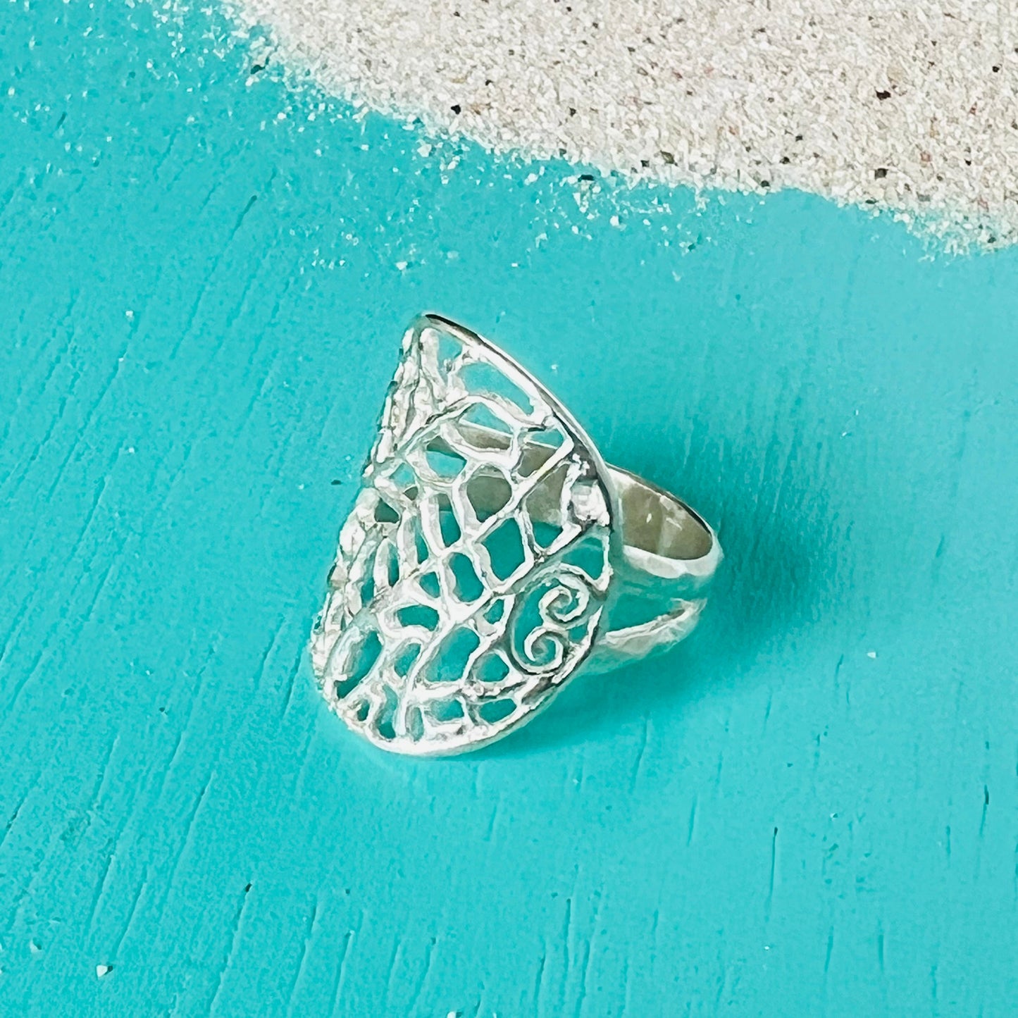 Silver ring with intricate design on a turquoise surface