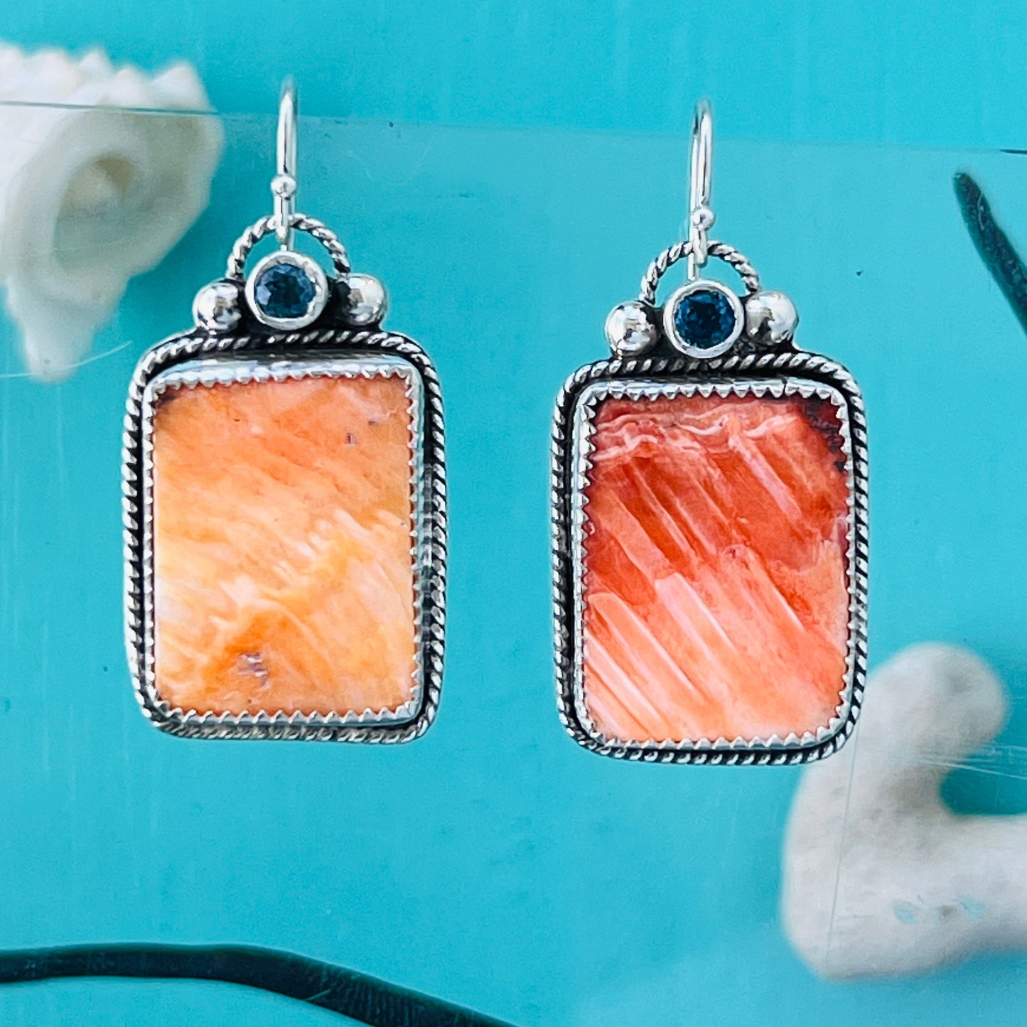 Pair of earrings with orange stone and silver frame on a blue background