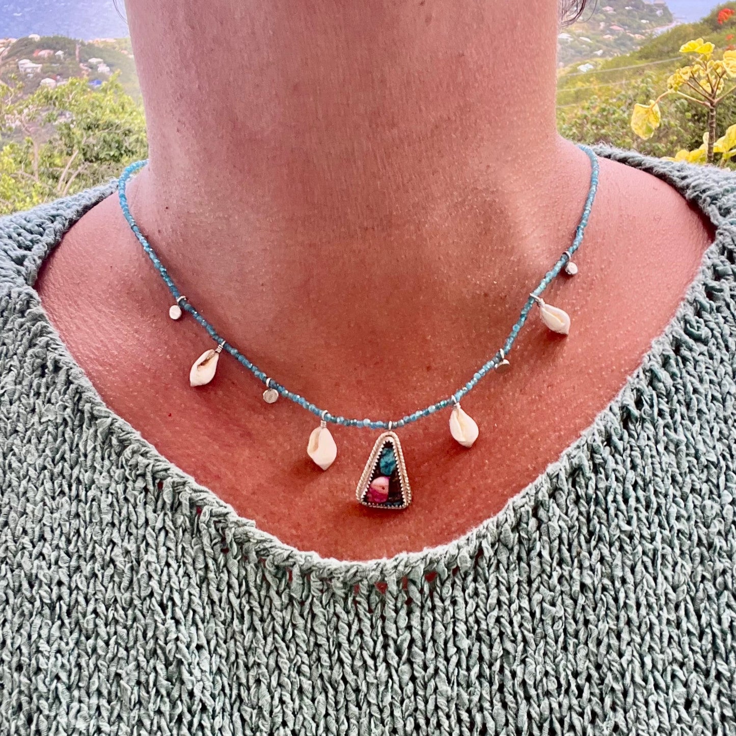 Necklace with a pendant worn by a person against a scenic background