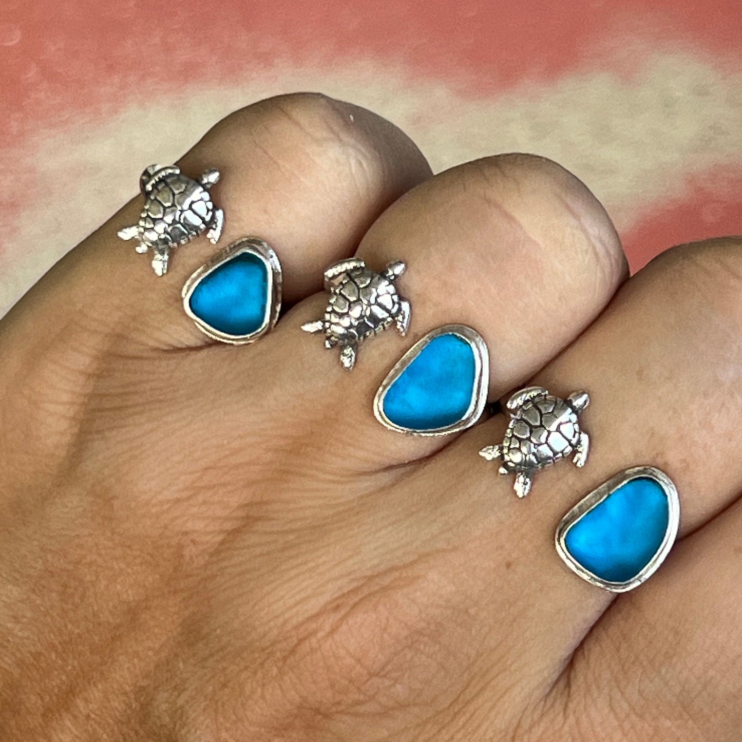 Finger wearing multiple turtle-shaped rings with blue stones on a blurred background