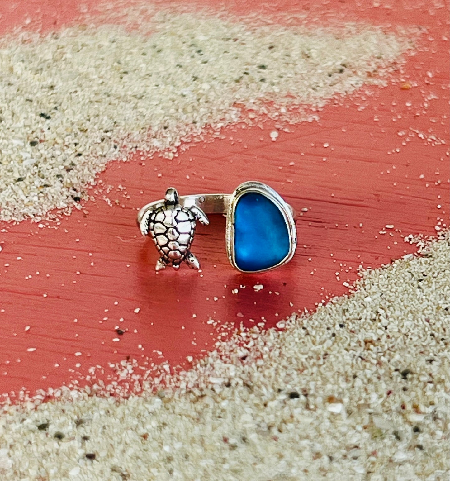 Ring with blue stone and turtle charm on a sandy surface