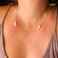 A close-up of a person's neck and chest wearing a delicate gold chain necklace with three irregular white baroque pearls and small clear stones.