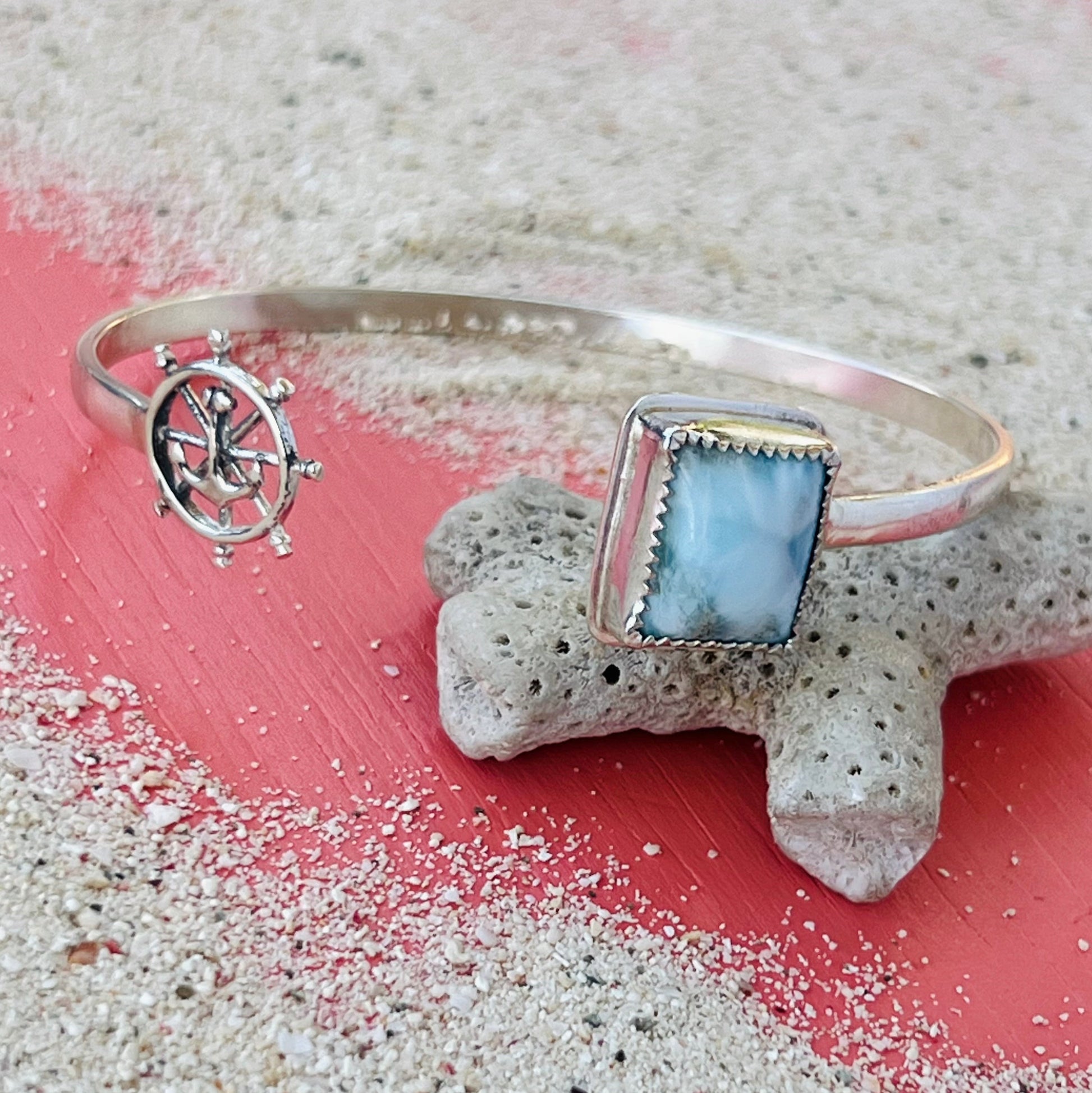 Silver bracelet with blue stone and ship wheel charm on a textured surface