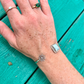 Hand wearing a silver bracelet with a turquoise background