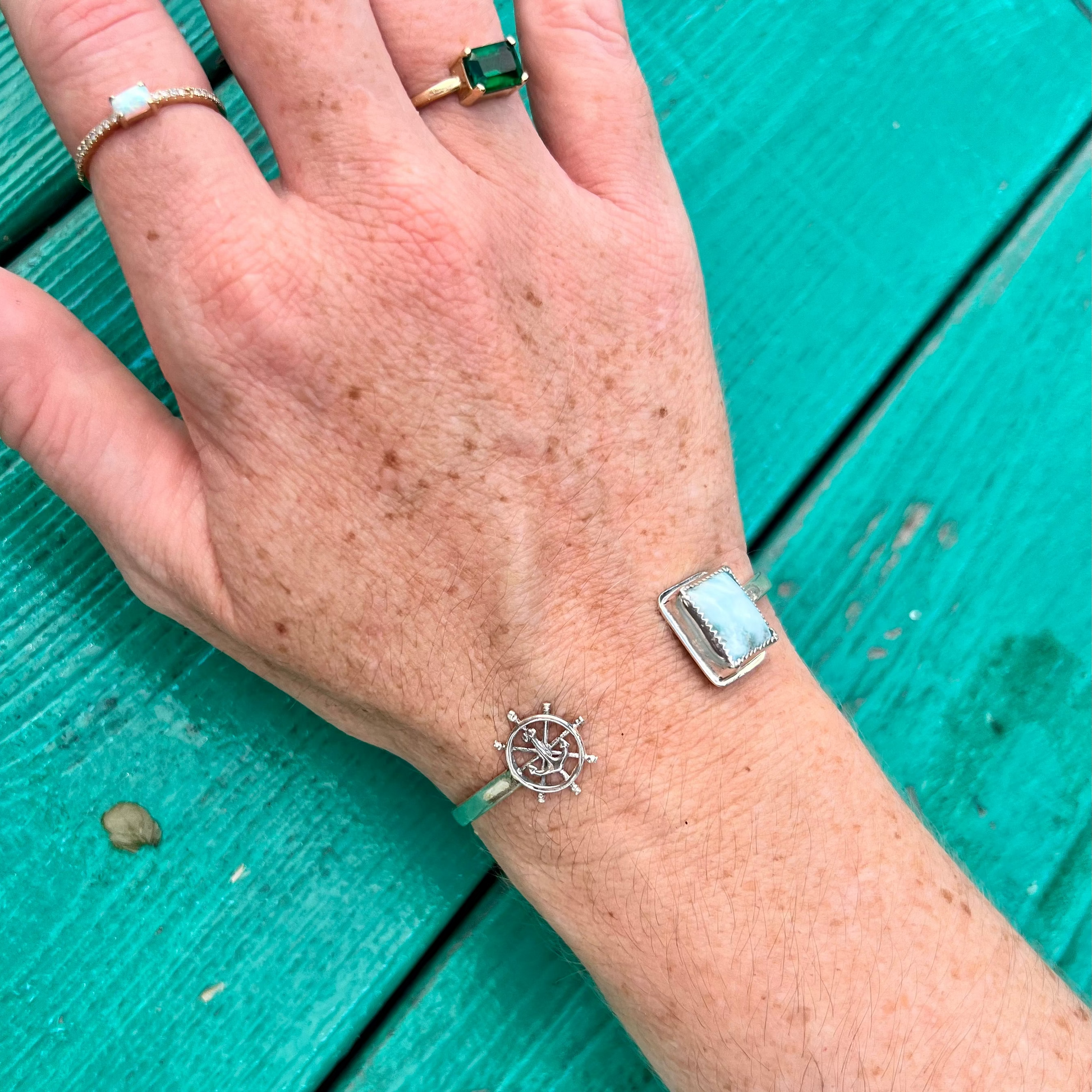 Hand wearing a silver bracelet with a turquoise background