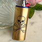 Brass lighter with skull and crossbones design on a light-colored surface.