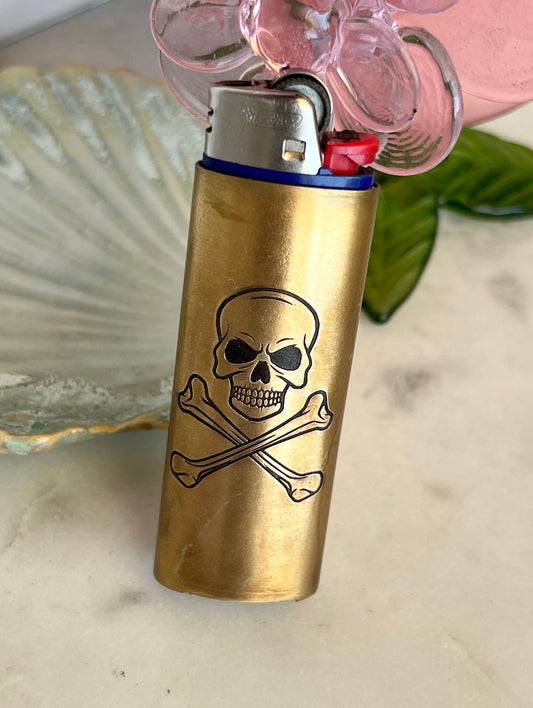 Brass lighter with skull and crossbones design on a light-colored surface.
