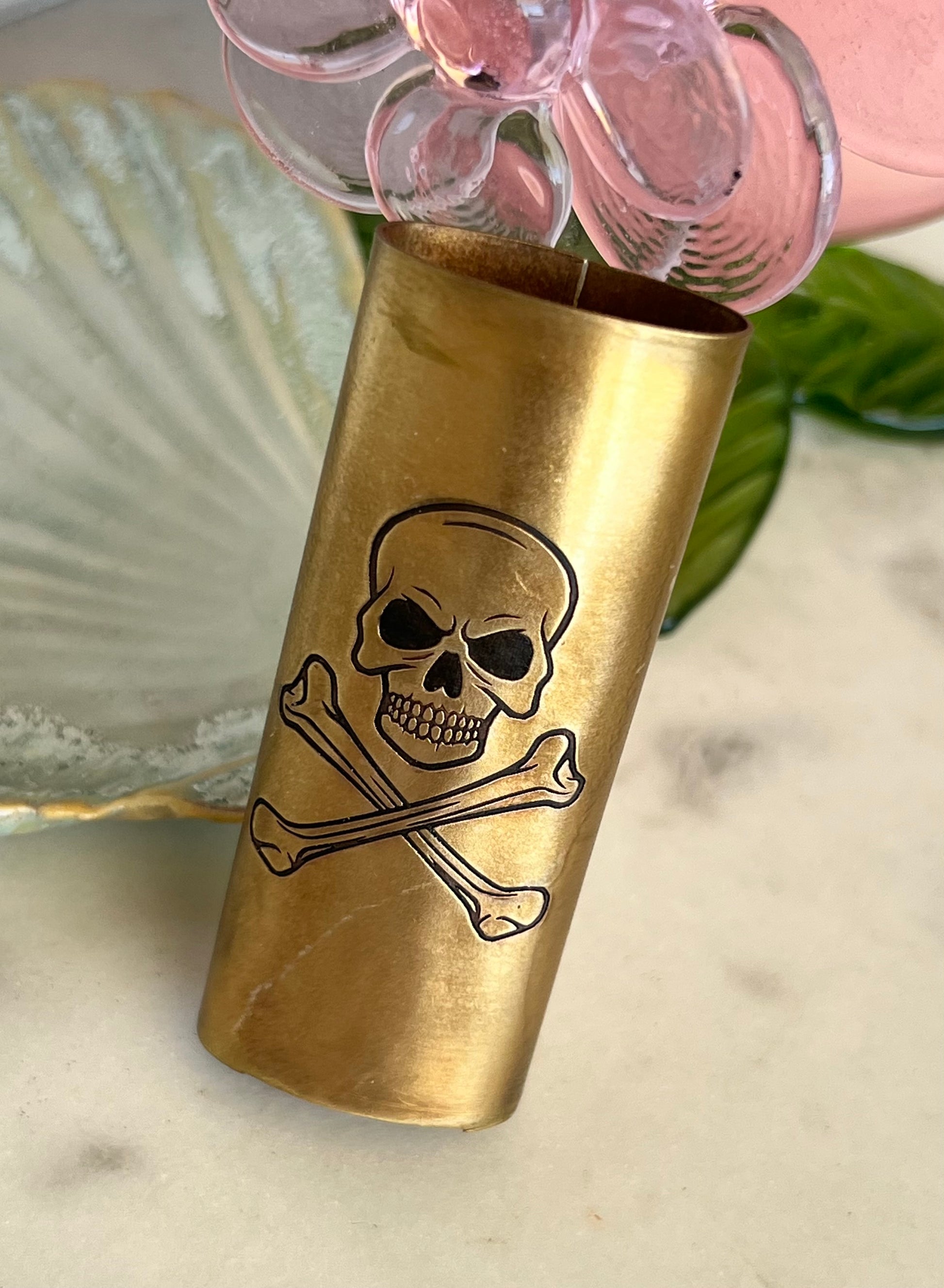 Brass shot glass with skull and crossbones design on a marble surface