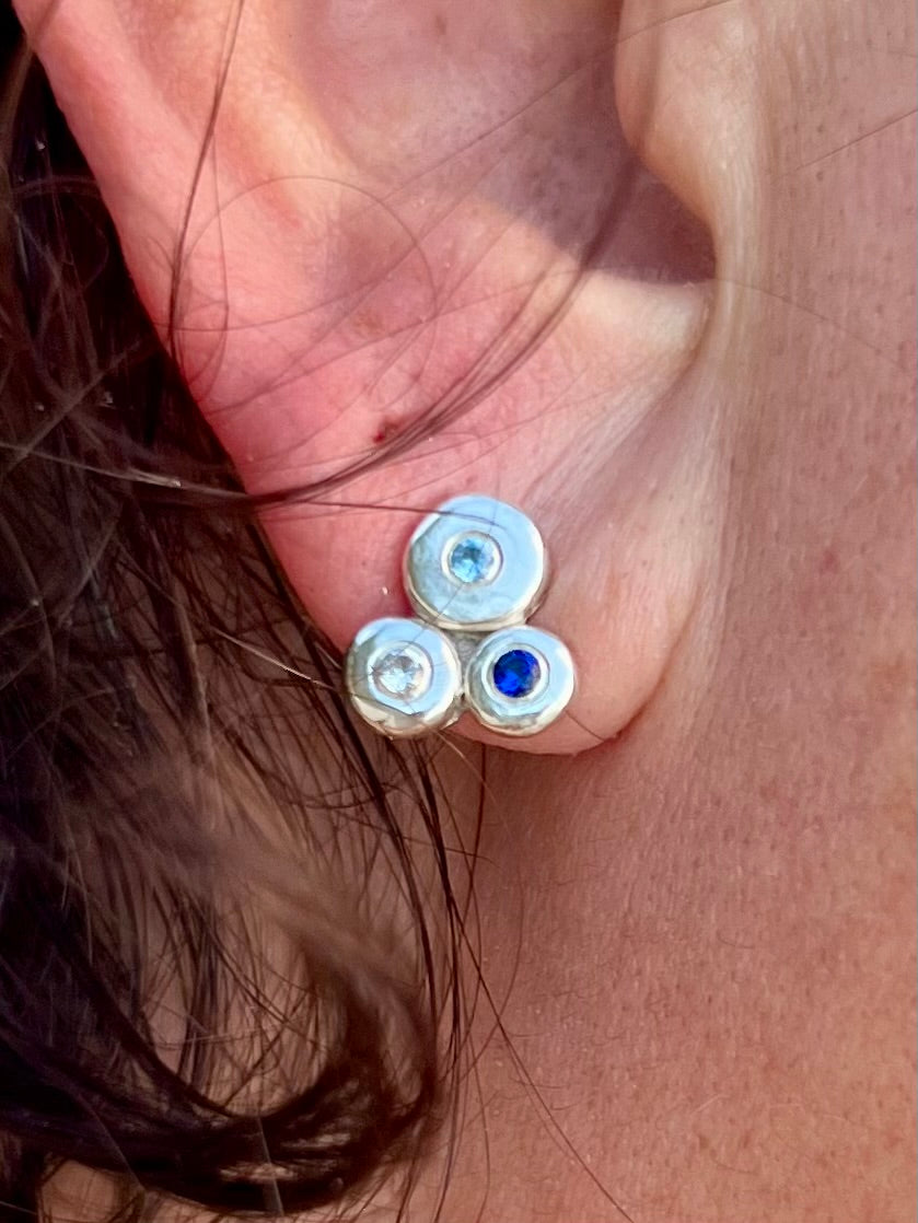 Close-up of an earring with three gemstones worn on an ear.