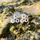 Set of small silver and gold earrings with blue stones on a textured rock surface