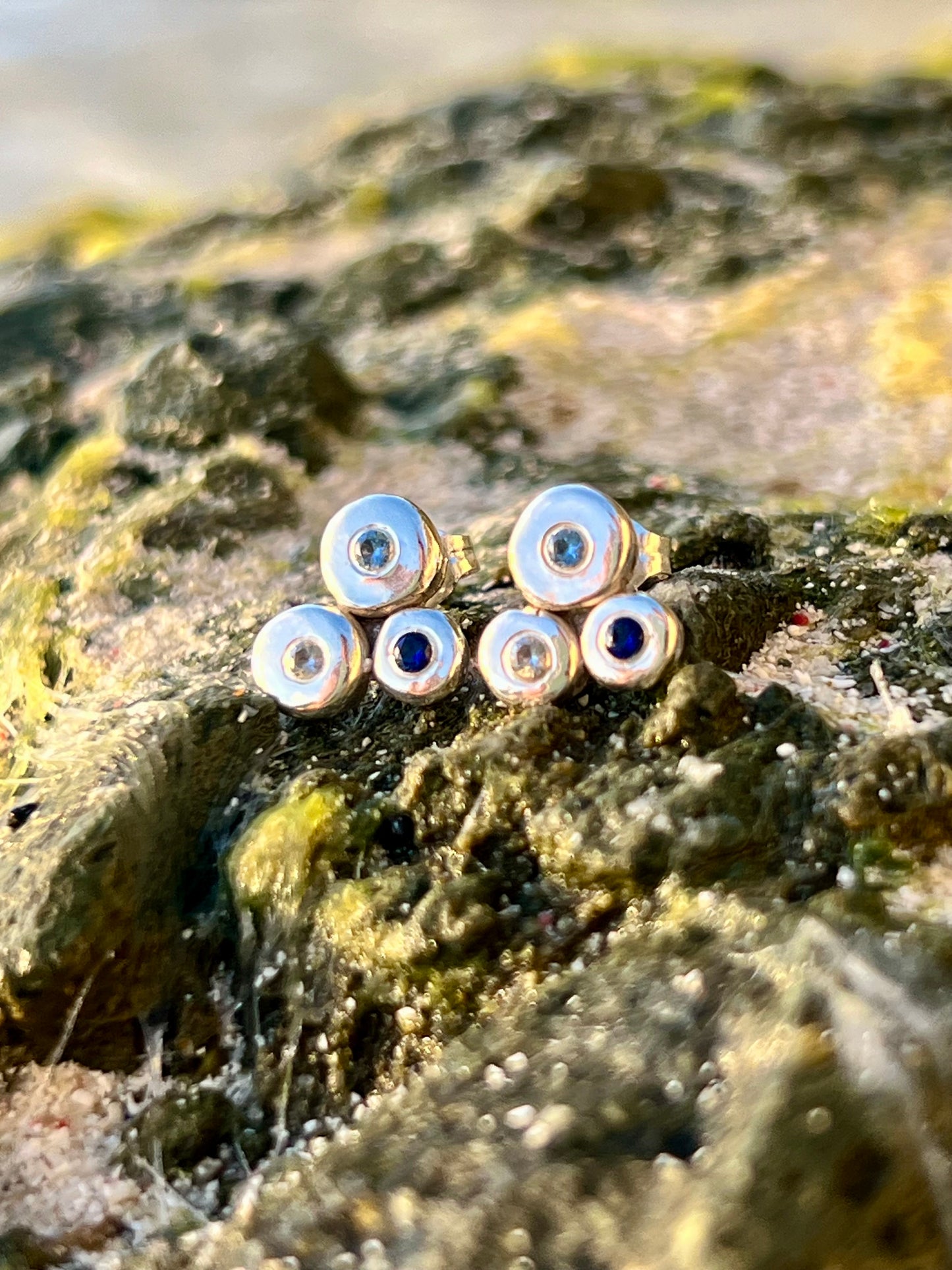 Set of small silver and gold earrings with blue stones on a textured rock surface