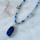 Necklace with blue pendant and beaded chain on a marble surface