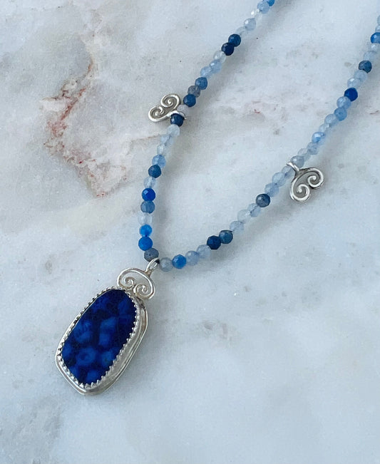 Necklace with blue pendant and beaded chain on a marble surface
