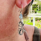 Earring with a mermaid design worn by a person, with a blurred outdoor background.