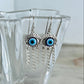 Silver earrings with blue eye design in a clear glass vase on a light background