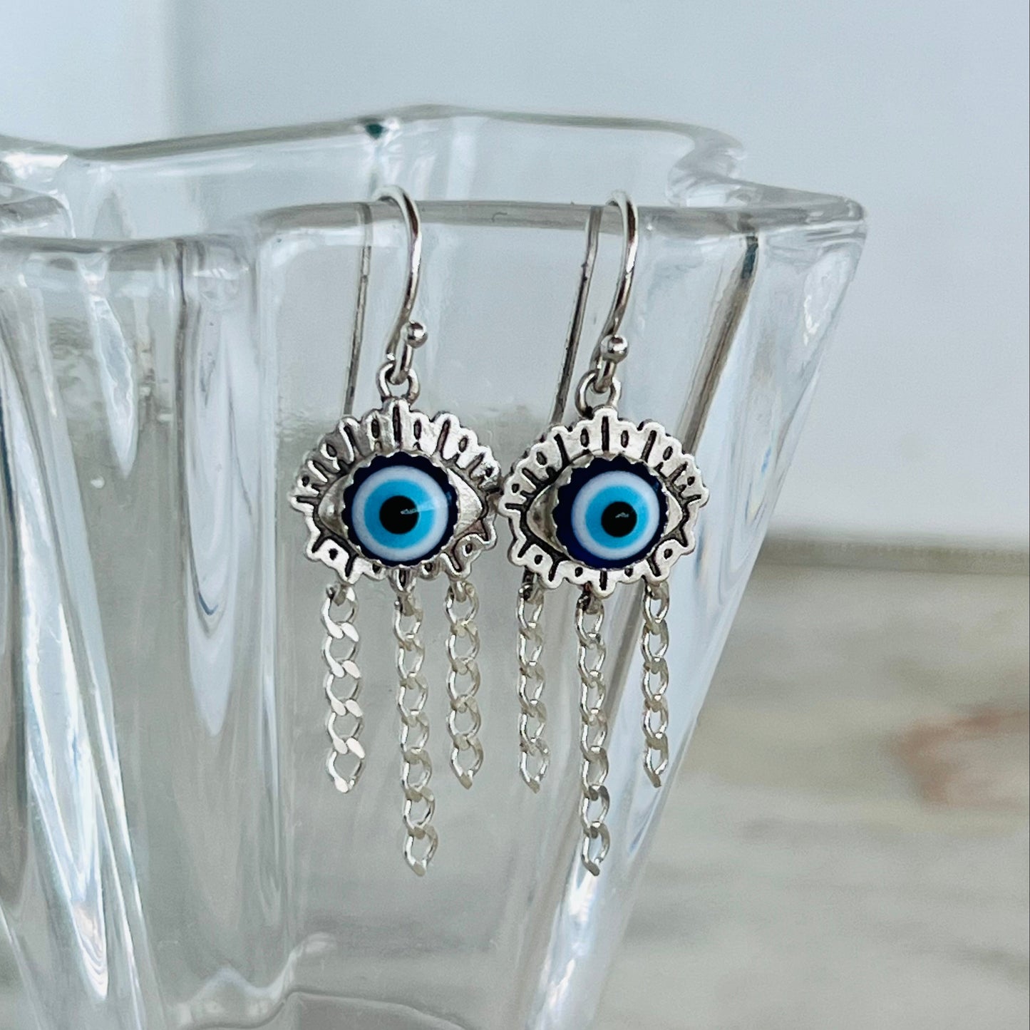 Silver earrings with blue eye design in a clear glass vase on a light background