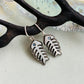 A pair of silver fish skeleton drop earrings with small blue stone accents, displayed on a dark branch against a light textured background.