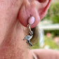 Close-up of an ear wearing a pink stone and flamingo charm earring with a blurred outdoor background.