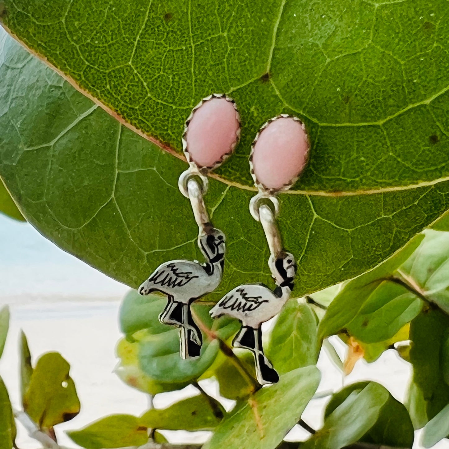Pink oval earrings with flamingo charms on a green leaf background