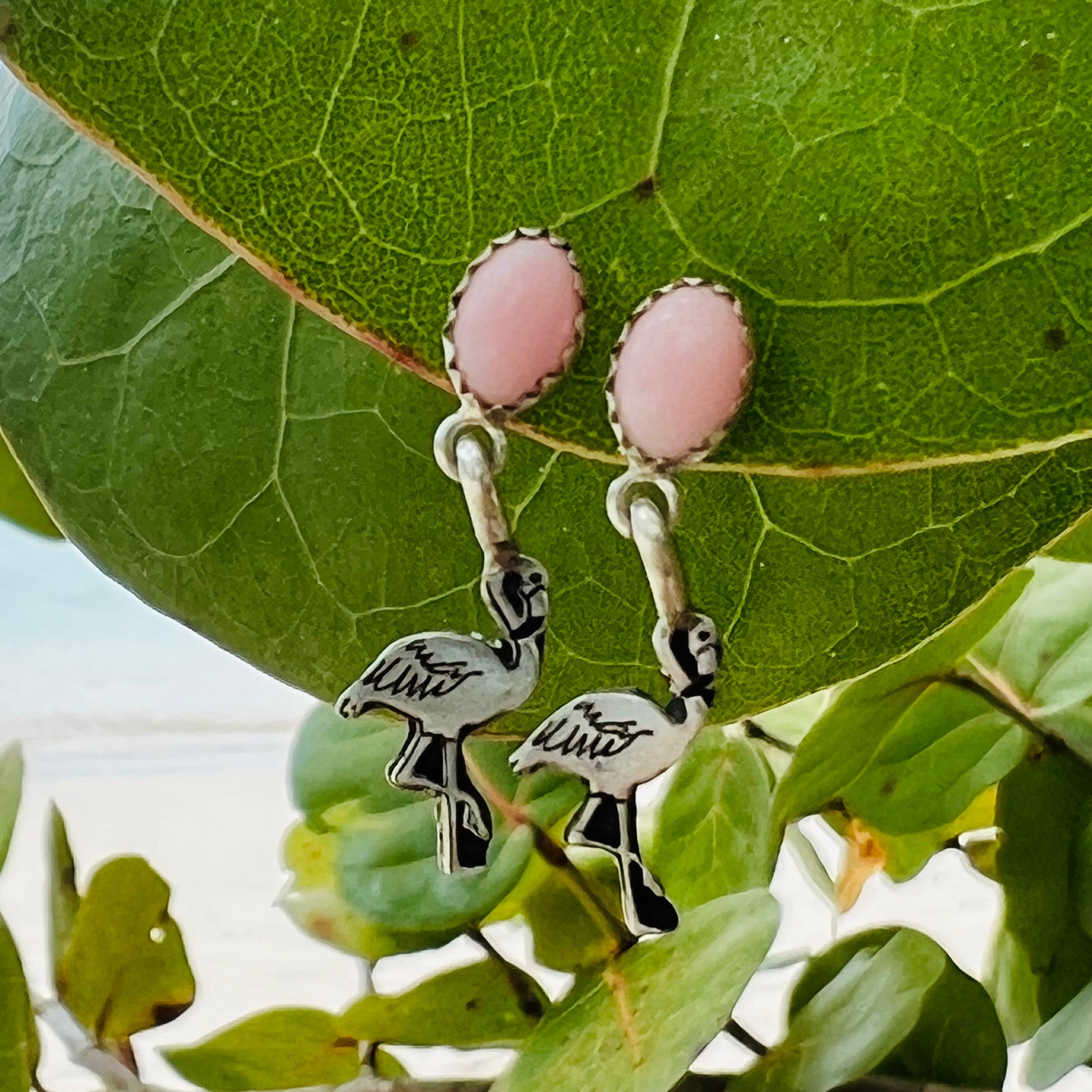 Pink oval earrings with flamingo charms on a green leaf background