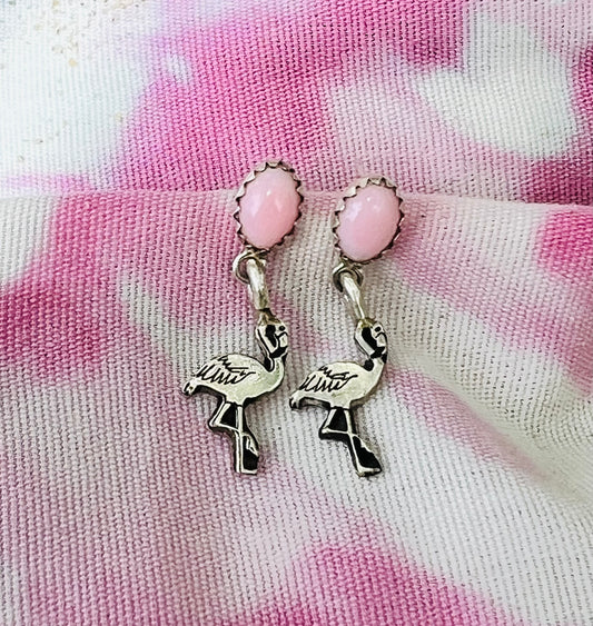 Flamingo-shaped charms with pink beads on a pink and white patterned fabric background