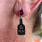 Close-up of an ear with a black and silver earring featuring a skull and 'Rum' text.
