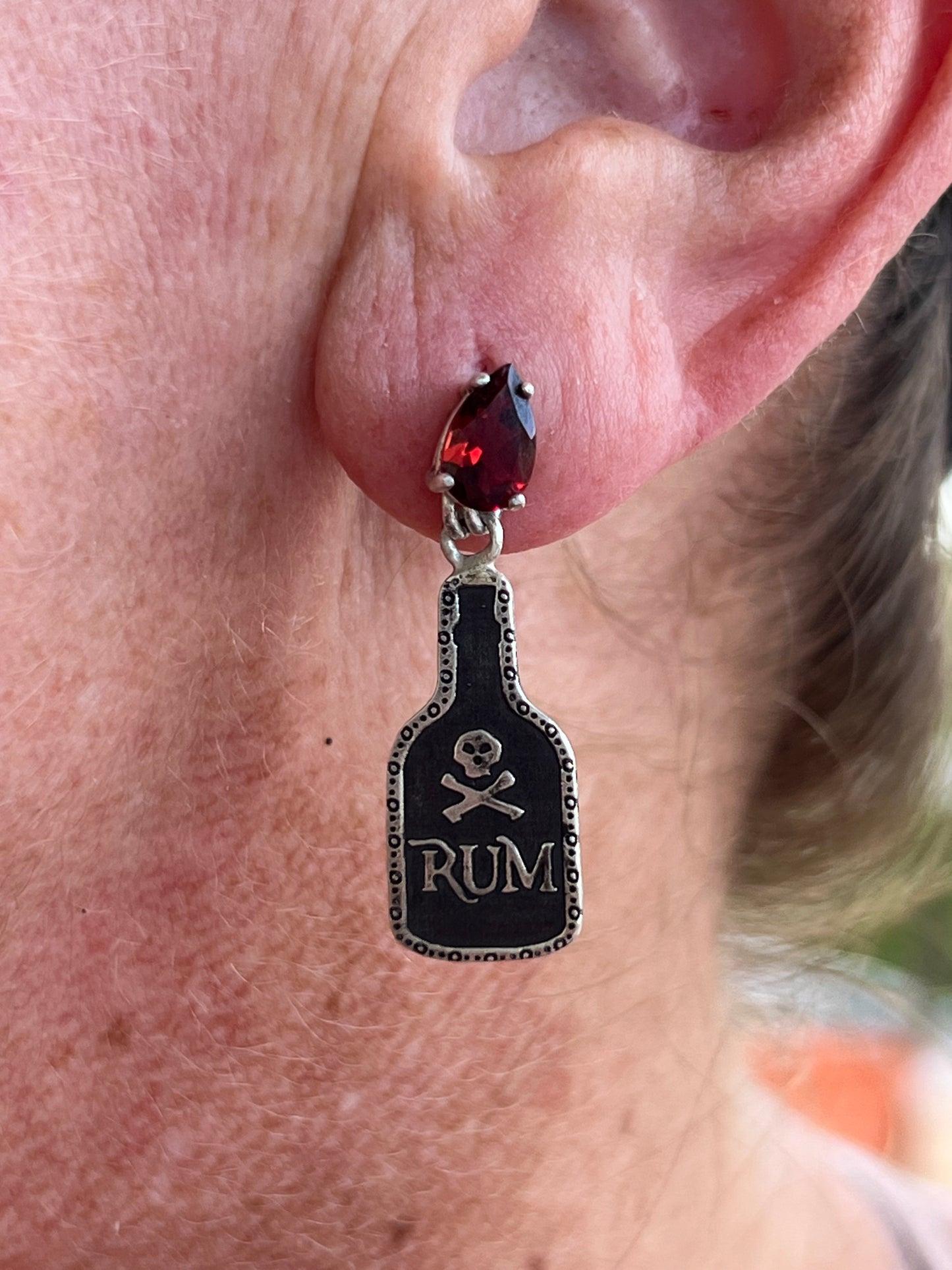 Close-up of an ear with a black and silver earring featuring a skull and 'Rum' text.