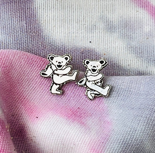 Two bear-shaped earrings on a tie-dye fabric background