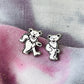 Two silver bear-shaped earrings on a textured fabric background