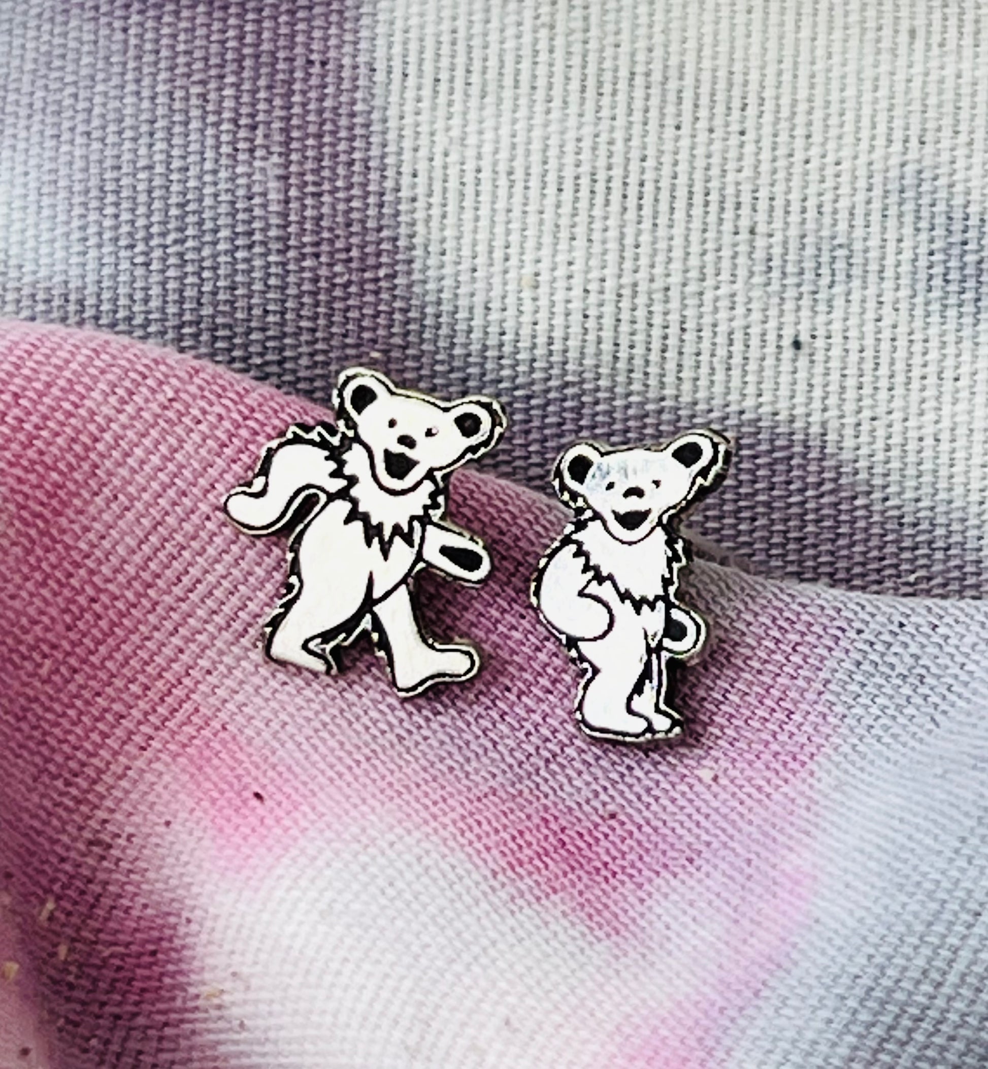 Two silver bear-shaped earrings on a textured fabric background