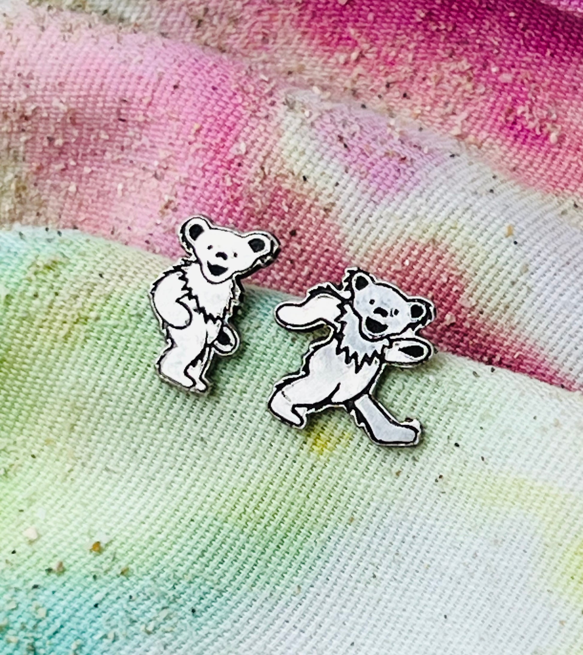 Two dancing bear earrings on a tie-dye fabric background