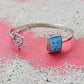 Silver bracelet with a blue stone and ship wheel charm on a sandy surface